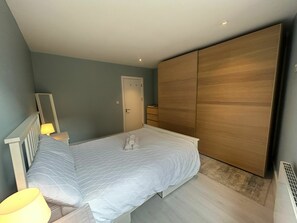 A bedroom with a bed, a nightstand, a lamp, a wardrobe, and a door. - Stylish 2BDR House with 2 Bathrooms Garden (Dublin)