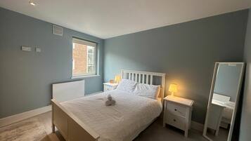 A bedroom with a bed, bedside tables, a mirror, and a window.