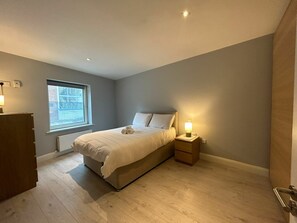 Ein Schlafzimmer mit Bett, Nachttisch, Fenster und Heizkörper.