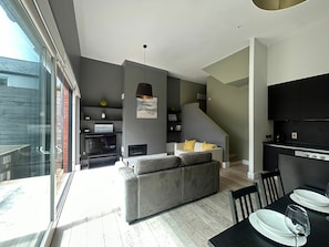 A modern living space with a grey sofa, a dining table with plates and a glass, and a kitchen area. - Stylish 2BDR House with 2 Bathrooms Garden (Dublin)