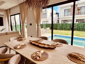 A modern dining area with a pool view, large windows, and a minimalist design. - Welcome to Villa Lina (Punta Cana)