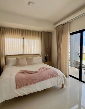 A modern bedroom with a large bed, a view of the outdoors, and a sliding glass door. - Welcome to Villa Lina (Punta Cana)