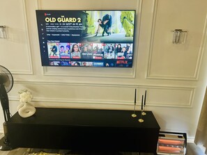Seinälle asennettu televisio, jonka näytöllä näkyy Netflixin käyttöliittymä ja siinä elokuva »The Old Guard 2» sekä muita ohjelmia.