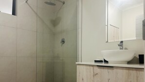 A modern bathroom with a shower, a sink, and a mirror. - Cozy Apartment in the heart of Joburg. (Midrand)