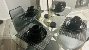 A round glass table with black plates and cups, black chairs, and a black and white patterned placemat. - Cozy Apartment in the heart of Joburg. (Midrand)