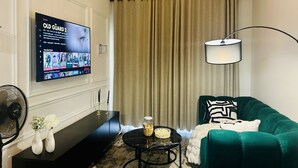 A living room with a TV, a sofa, a coffee table, a lamp, and a fan. - Cozy Apartment in the heart of Joburg. (Midrand)