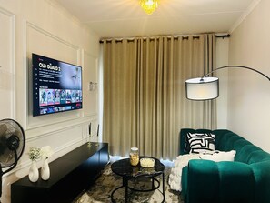 Ein Wohnzimmer mit Fernseher, einer Couch, einem Couchtisch, einer Lampe und einem Ventilator.