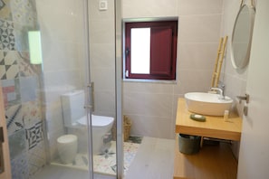 Ein Badezimmer mit Glasdusche, Toilette, Waschbecken mit Spiegel und einem Fenster mit rotem Rollo.