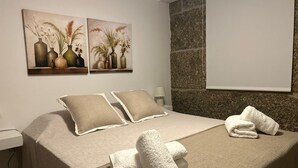 En snyggt bäddad säng med ett beige överkast, två kuddar och hopvikta handdukar på en matt med struktur.