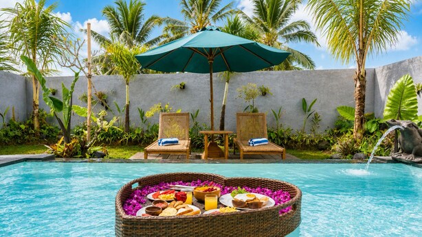 A pool with a floating basket containing food and drinks, surrounded by lounge chairs and a palm tree. - Togog Sebatu Villa (Gianyar)