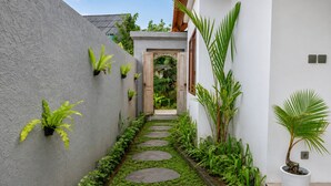 A narrow pathway with stepping stones, surrounded by lush greenery and potted plants. - Togog Sebatu Villa (Gianyar)