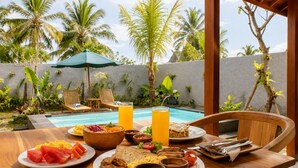 A breakfast setting with a pool view, wooden furniture, and tropical plants. - Togog Sebatu Villa (Gianyar)