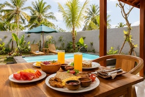 Cenário de café da manhã com vista para piscina, móveis de madeira e plantas tropicais.