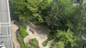 Vista aérea de una zona ajardinada con senderos sinuosos, rodeada de abundante vegetación y contigua a un estacionamiento con varios coches.