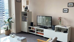 Una sala de estar moderna con un televisor de pantalla plana, un mueble blanco para equipo audiovisual, una planta en maceta y un sillón cómodo.