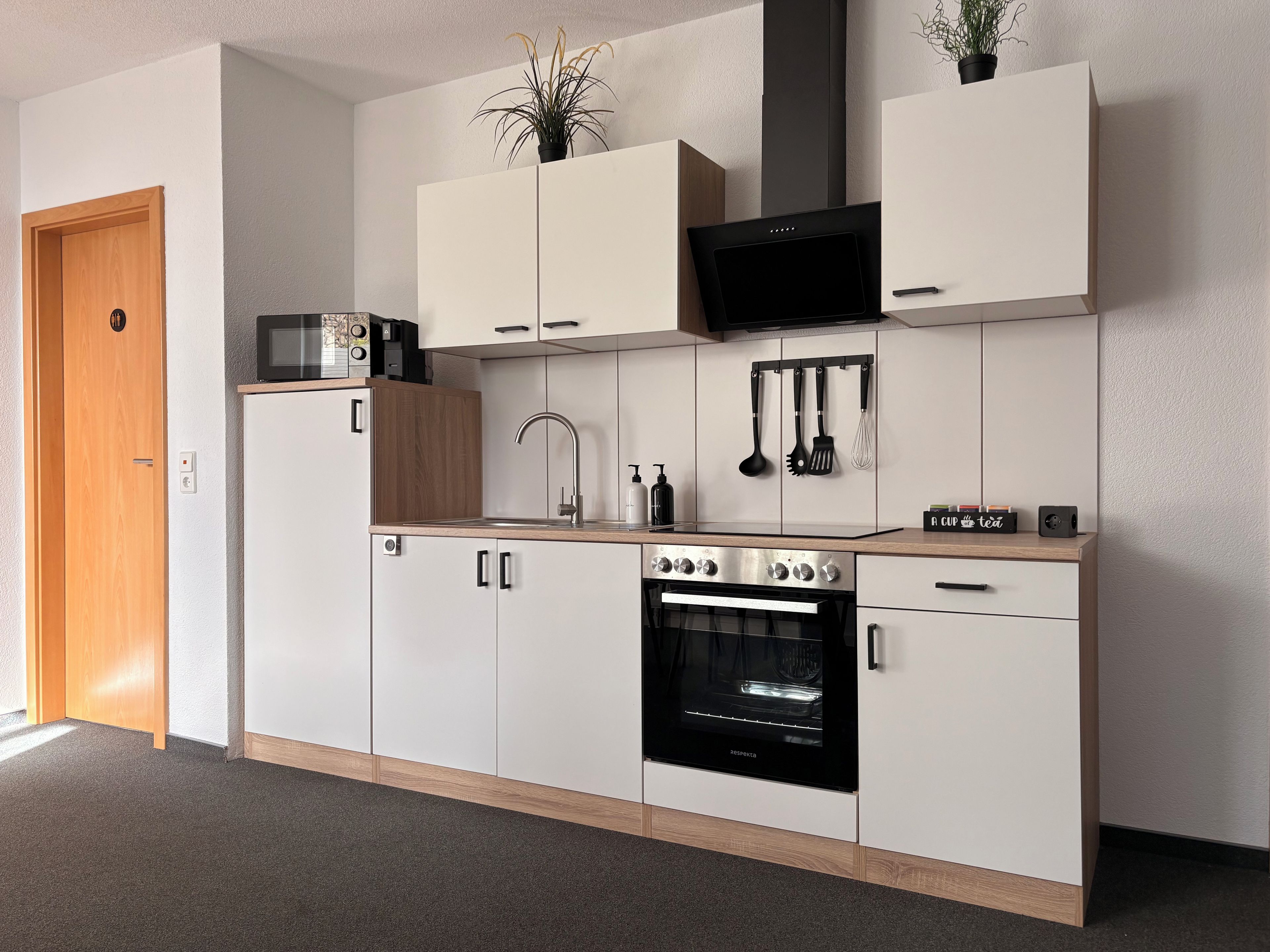 A modern kitchen with white cabinets, a built-in oven, a microwave, and a sink.