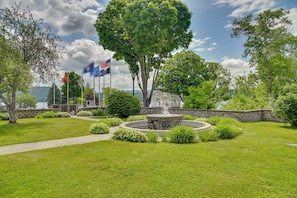 Ein angelegter Garten mit einem Brunnen, Flaggen und Blick auf ein Gewässer.