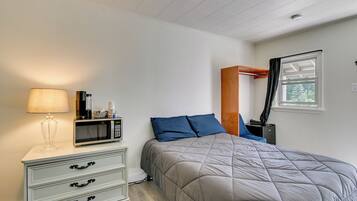 A bedroom with a bed, a bedside table with a lamp, a microwave, and a window with curtains.