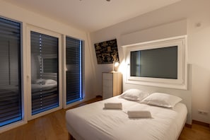 Une chambre à coucher comprenant un lit, une commode, une table de chevet et une fenêtre avec des stores.