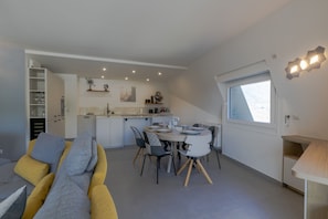 Une cuisine moderne avec des meubles blancs, un coin repas doté d’une table ronde et de chaises, et une grande fenêtre laissant entrer la lumière naturelle.