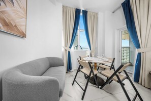 Ein modernes Zimmer mit einem grauen Sofa, einem runden Tisch mit Stühlen und Blick nach draußen.