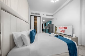 Ein Hotelzimmer mit Bett, Fernseher, Schreibtisch und Blick auf die Küche.