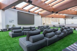 Ein modernes Freiluftkino mit einer großen Leinwand, mehreren grauen Sofas und einem grünen Rasenbelag.