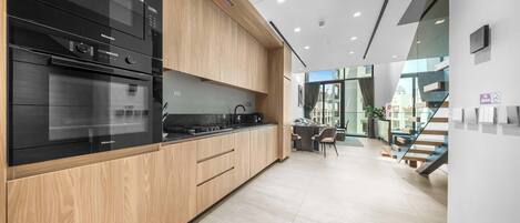 A modern kitchen with built-in appliances, wooden cabinetry, and a view to a dining area.