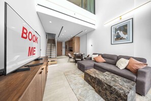 Ein modernes Wohnzimmer mit einer Couch, einem Couchtisch und einem Fernseher, der 'BOOK ME' anzeigt.