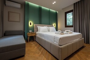 Ein modernes Hotelzimmer mit einem großen Bett, einem Nachttisch, einem Sessel und einem Fenster mit Vorhängen.