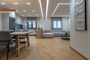 Ein modernes Wohnzimmer mit Essbereich, einer Küche im Hintergrund und einem großen abstrakten Gemälde an der Wand.