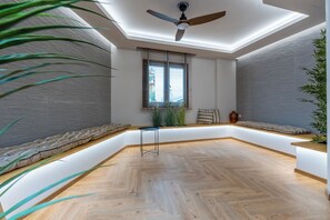 Ein modernes Interieur mit Deckenventilator, Dachfenster, Holzboden im Fischgrätmuster, einer Sitzecke mit Kissen und einem kleinen Tisch.