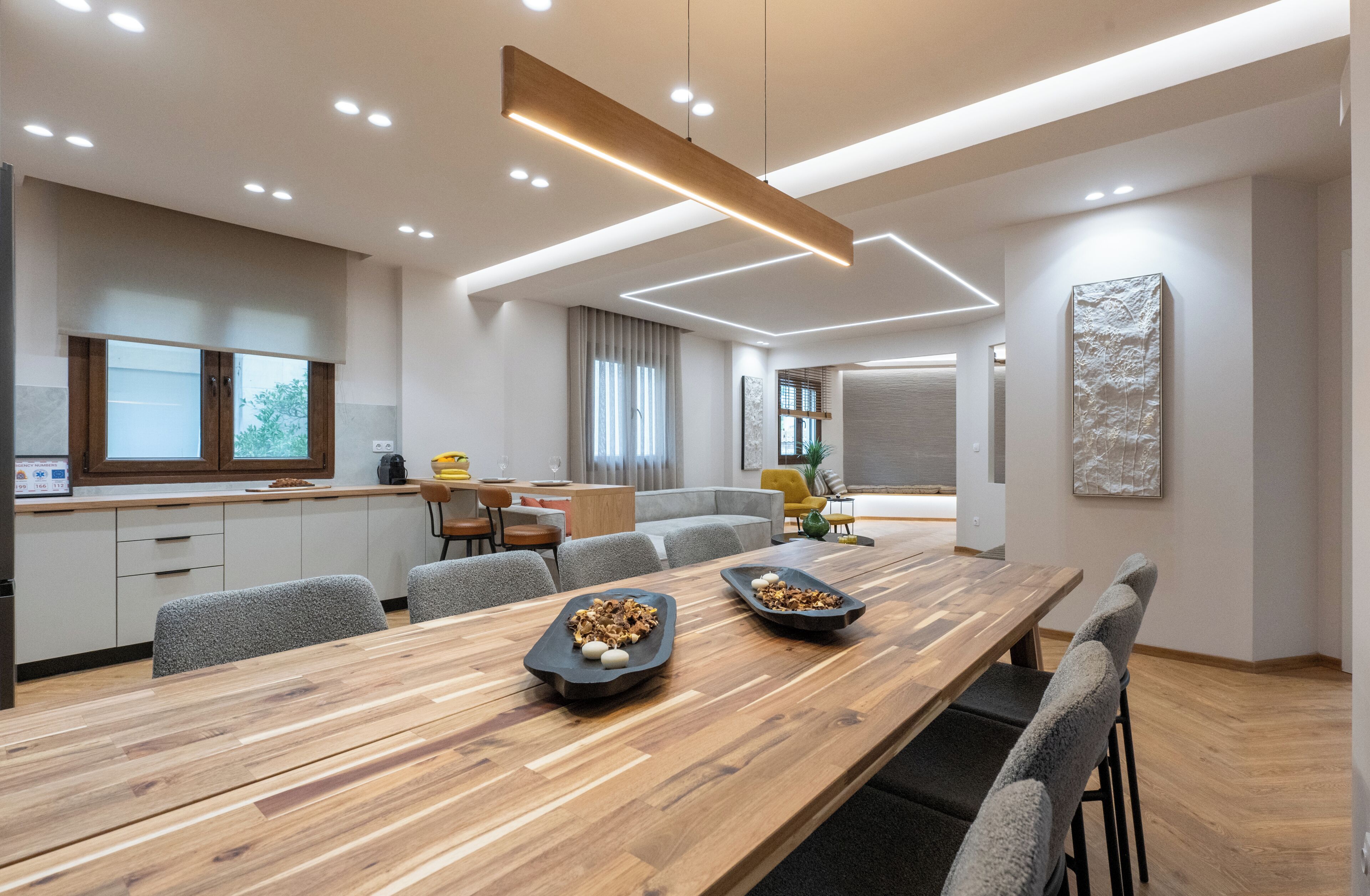 Eine moderne Küche mit Holztischplatte, einem Esstisch mit zwei schwarzen Servierplatten und einer Sitzecke mit Sofa und Sesseln.