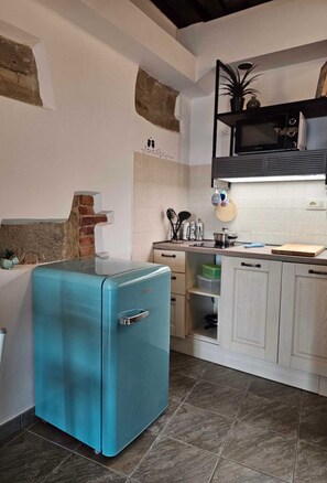 Eine kleine Küche mit einem blauen Kühlschrank, weißen Schränken und einem gefliesten Boden.