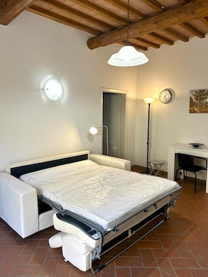 Ein Schlafzimmer mit einem Bett, einem Schreibtisch, einem Stuhl, einer Lampe, einer Uhr und einer Tür.