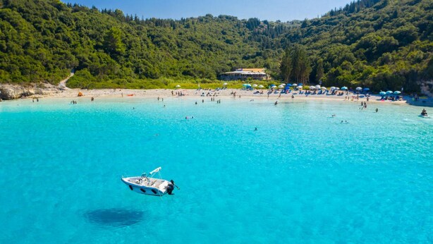 A beach with clear turquoise water, a boat, and a building in the background.