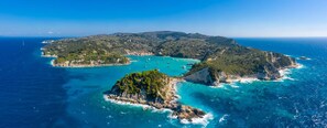 An aerial view of a coastal area with clear turquoise waters, rocky outcrops, and lush green hills. - Niki Studio Dio in Lakka (Paxos)