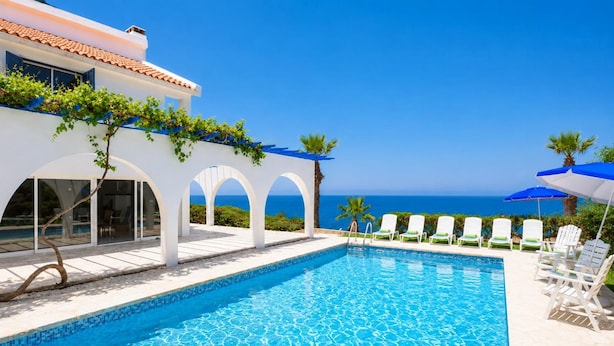 Ein Poolbereich mit freiem Blick auf das Meer, weißen Bögen und Liegestühlen.