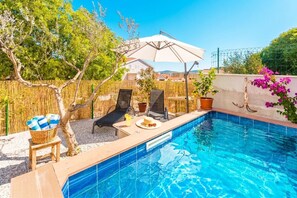Ein Schwimmbad mit Holzterrasse, Liegestühlen, einem Tisch mit einer Handtuchkorb und einer Pergola mit Sonnenschirm.