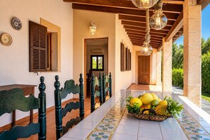 A covered outdoor dining area with a tiled floor, a long table, and a fruit basket. - Villa Sa Pleta in Mallorca (Son Servera)