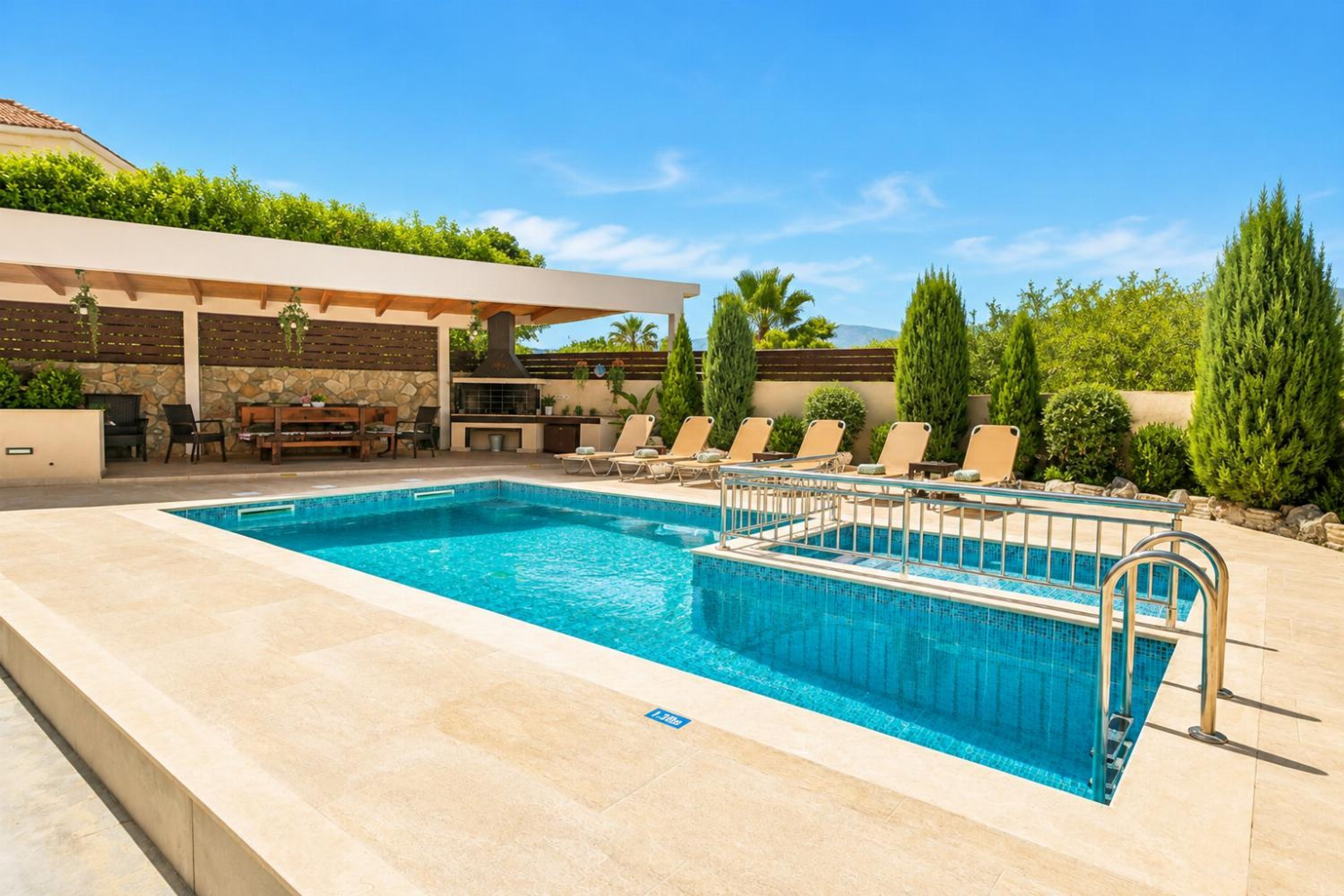 Une piscine rectangulaire bordée d’un muret en pierre, avec des chaises longues et un espace de détente abrité.