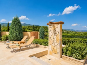 A patio with lounge chairs, a stone pillar, and a view of a vineyard. - Villa Maggie Alonia in Zakinthos (Zakynthos)