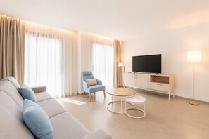 Un salon moderne comprenant un canapé, un fauteuil, un téléviseur, un meuble et une lampe.
