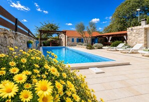 Ein Pool mit Steinmauer, einer Pergola und einem Gebäude mit rotem Dach.