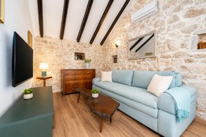 A room with a stone wall, a wooden dresser, a light blue sofa, a wooden coffee table, and a flat-screen TV. - Didini Dvori in Kru evo (Obrovac)