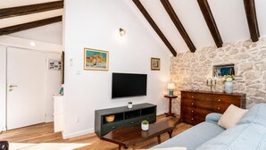 Ein Wohnzimmer mit Steinwand, Holzbalken, einem Fernseher, einer Couch, einem Couchtisch und einer Kommode.