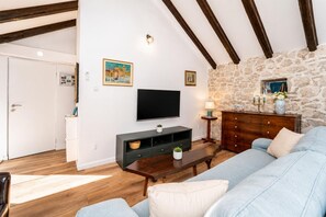 A living room with a stone wall, wooden beams, a TV, a sofa, a coffee table, and a dresser. - Didini Dvori in Kru evo (Obrovac)