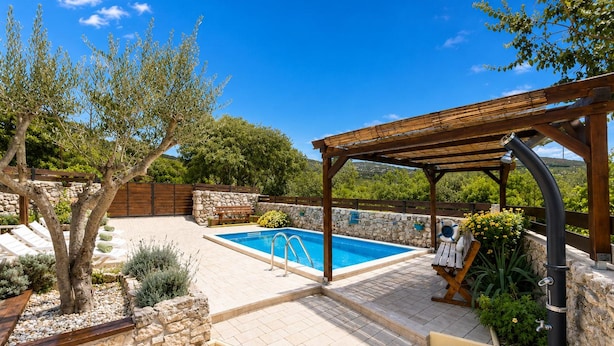 Ein Poolbereich mit einer Pergola, Steinmauern und Liegestühlen.