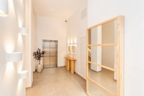 A modern hallway with a wooden-framed mirror, a wall-mounted light fixture, and a potted plant. - Ereza Residence 3 in Arrecife (Arrecife)