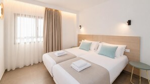 Ett hotellrum med två sängar, ett litet bord och ett fönster med gardiner.